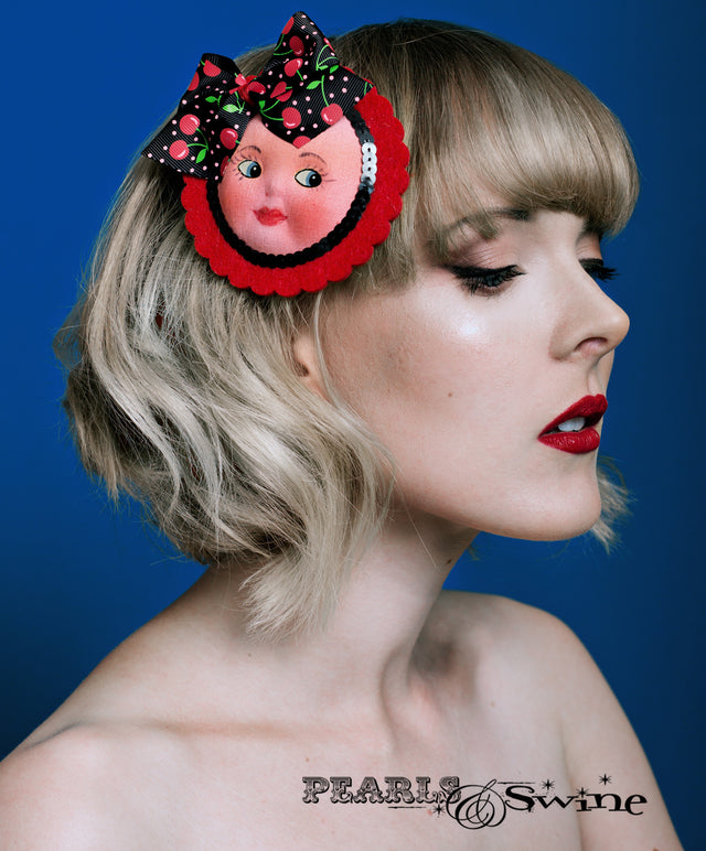 Cute vintage dollfaced hair clip, set on a red felt base and decorated with a black cherry covered bow and sequin